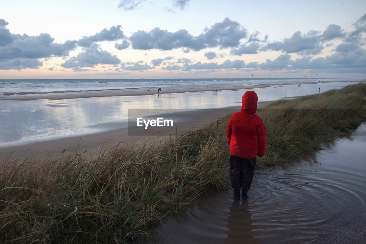 REAR VIEW OF WOMAN STANDING ON SHORE AGAINST SEA