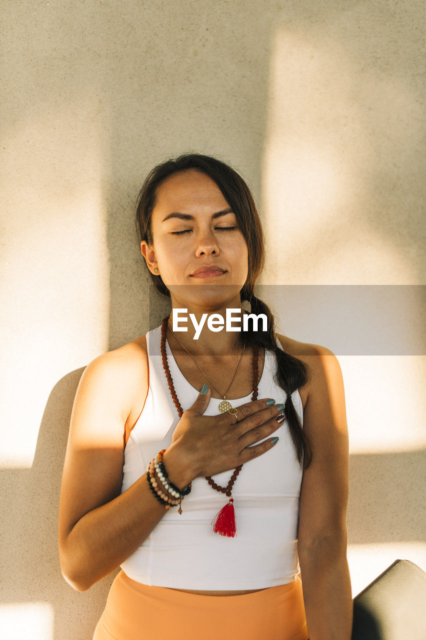 Woman with hand on chest standing against wall