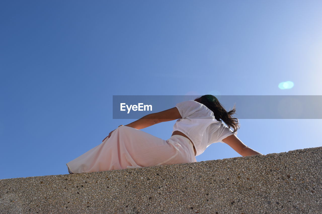 Low angle view of woman against clear blue sky