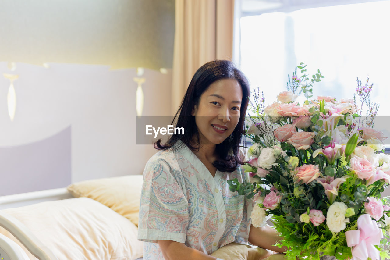 Woman patient smiling and holding a flower bouquet sitting on hospital bed.