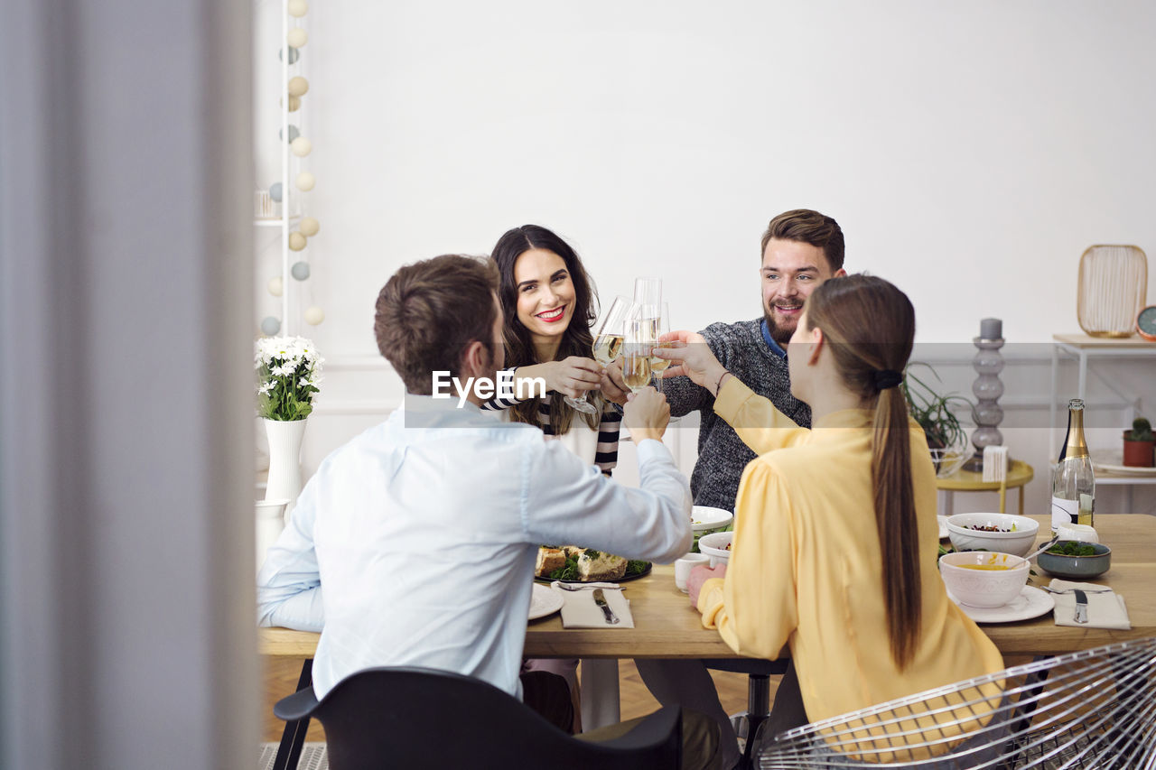 Happy friends toasting champagne flutes while sitting at dinning table in lunch party