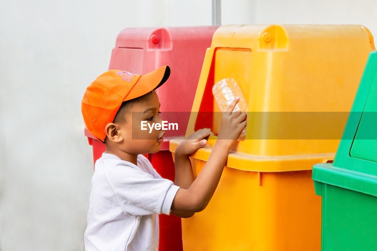 Side view of boy throwing plastic bottle in garbage bin