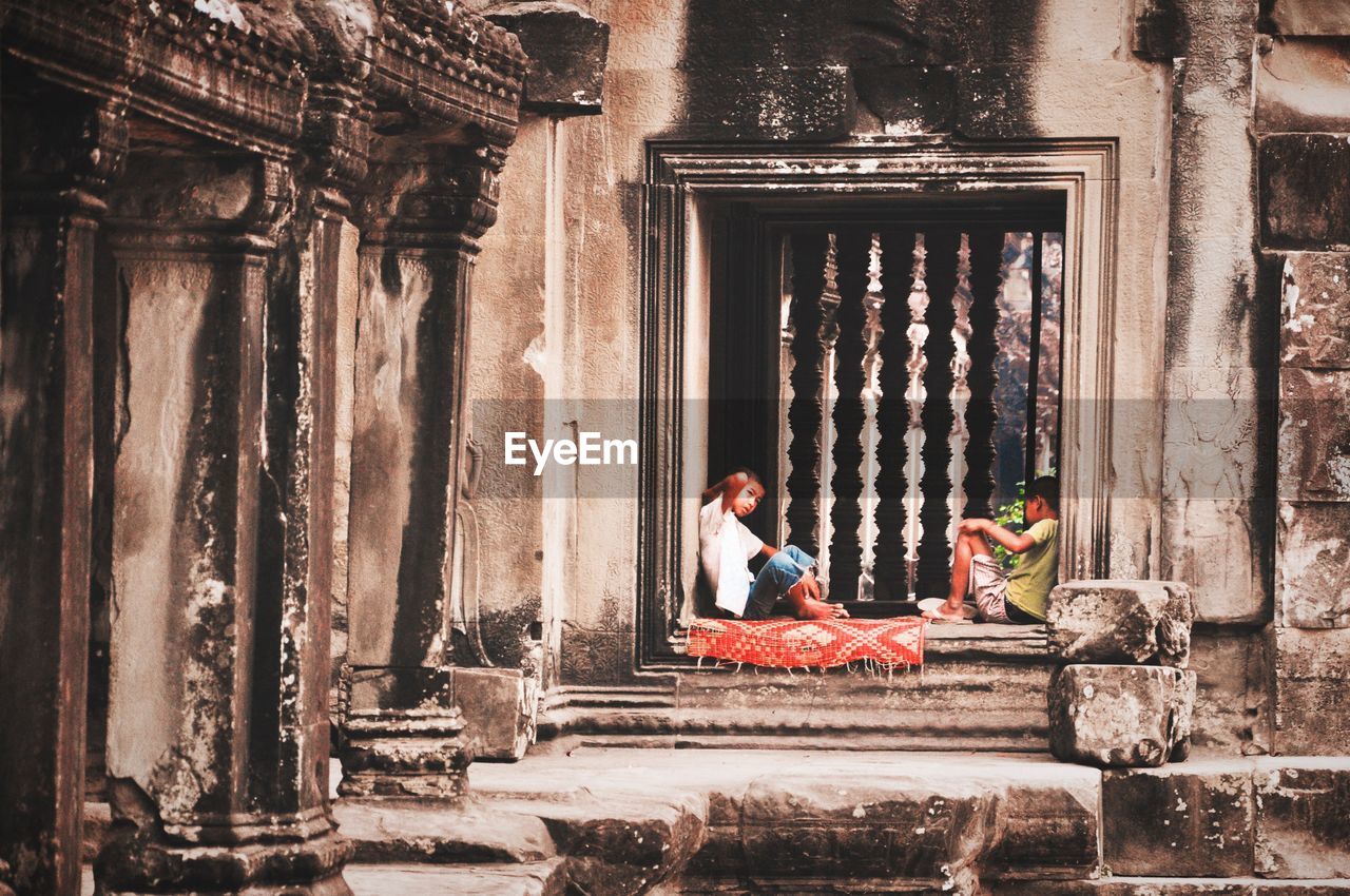 MAN SITTING ON OLD OUTSIDE TEMPLE BUILDING