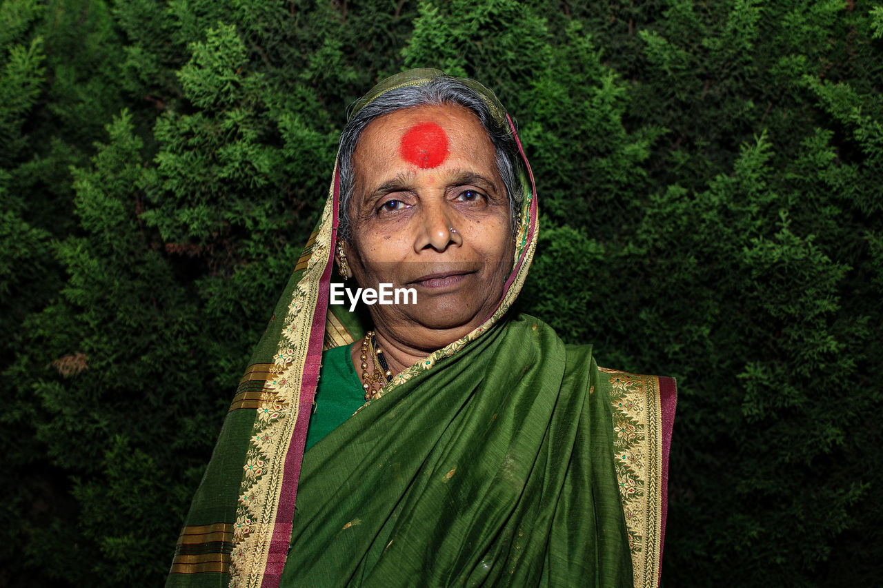 Portrait of smiling senior woman standing against trees