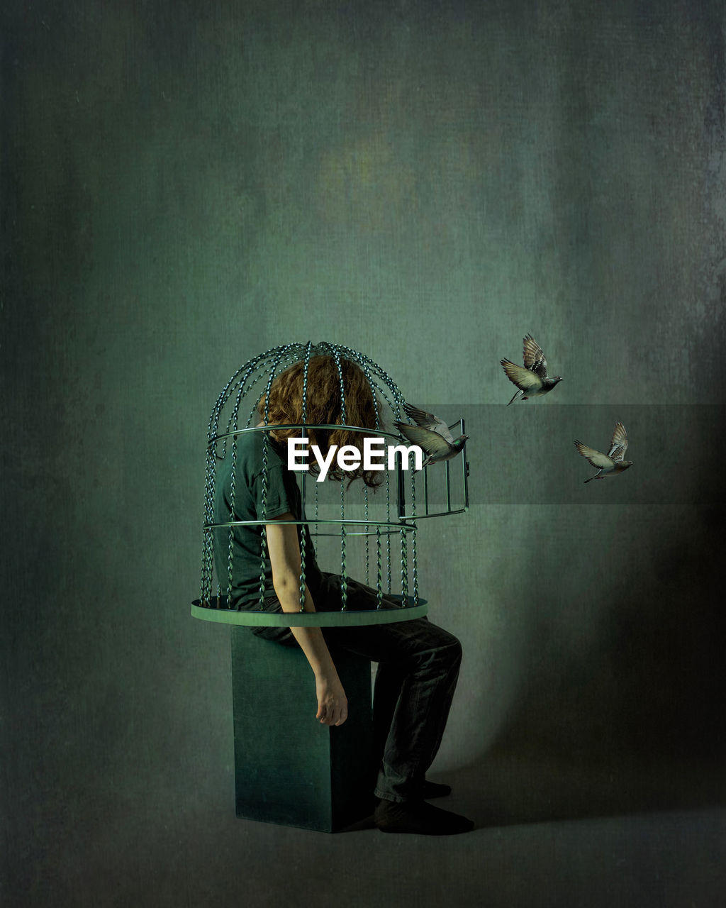 Rear view of a kid sitting in a cage against the wall with birds flying away