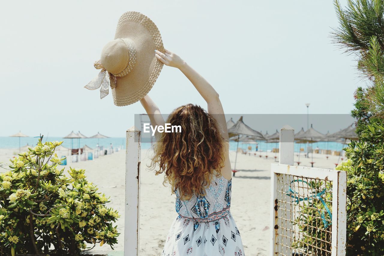 Rear view of woman with hat standing at beach against sky