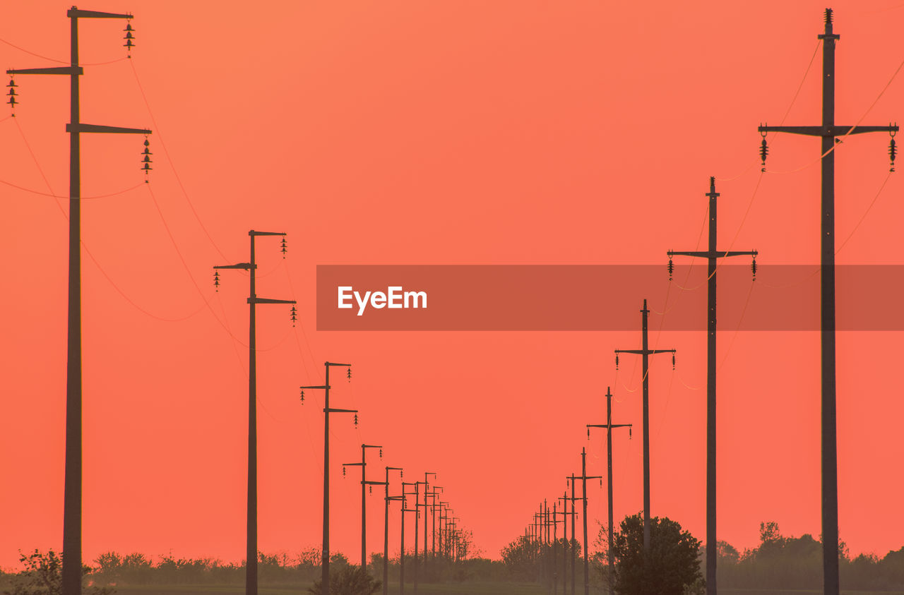 LOW ANGLE VIEW OF ELECTRICITY PYLONS AGAINST ORANGE SKY