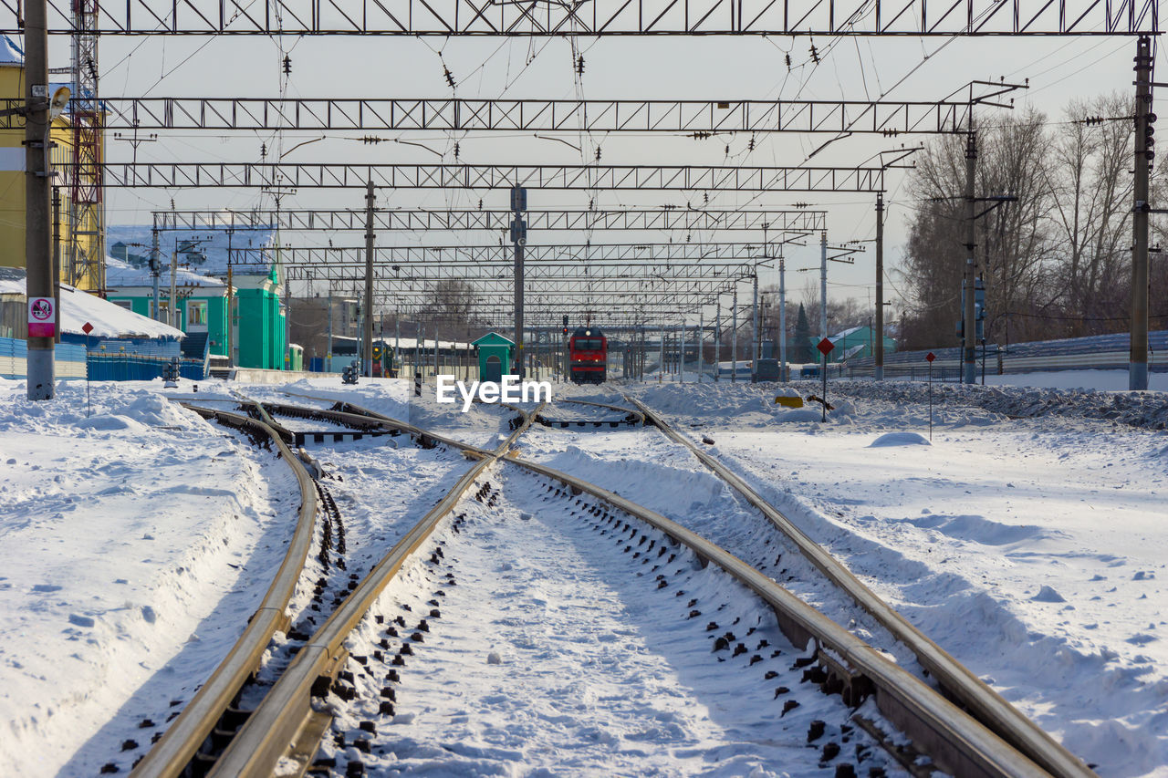 snow, winter, cold temperature, rail transportation, railroad track, transport, track, transportation, nature, mode of transportation, day, train, architecture, built structure, no people, vehicle, covering, the way forward, outdoors, railway, electricity, railroad station, frozen, travel, building exterior, electricity pylon, cable, sky, public transportation, white, city