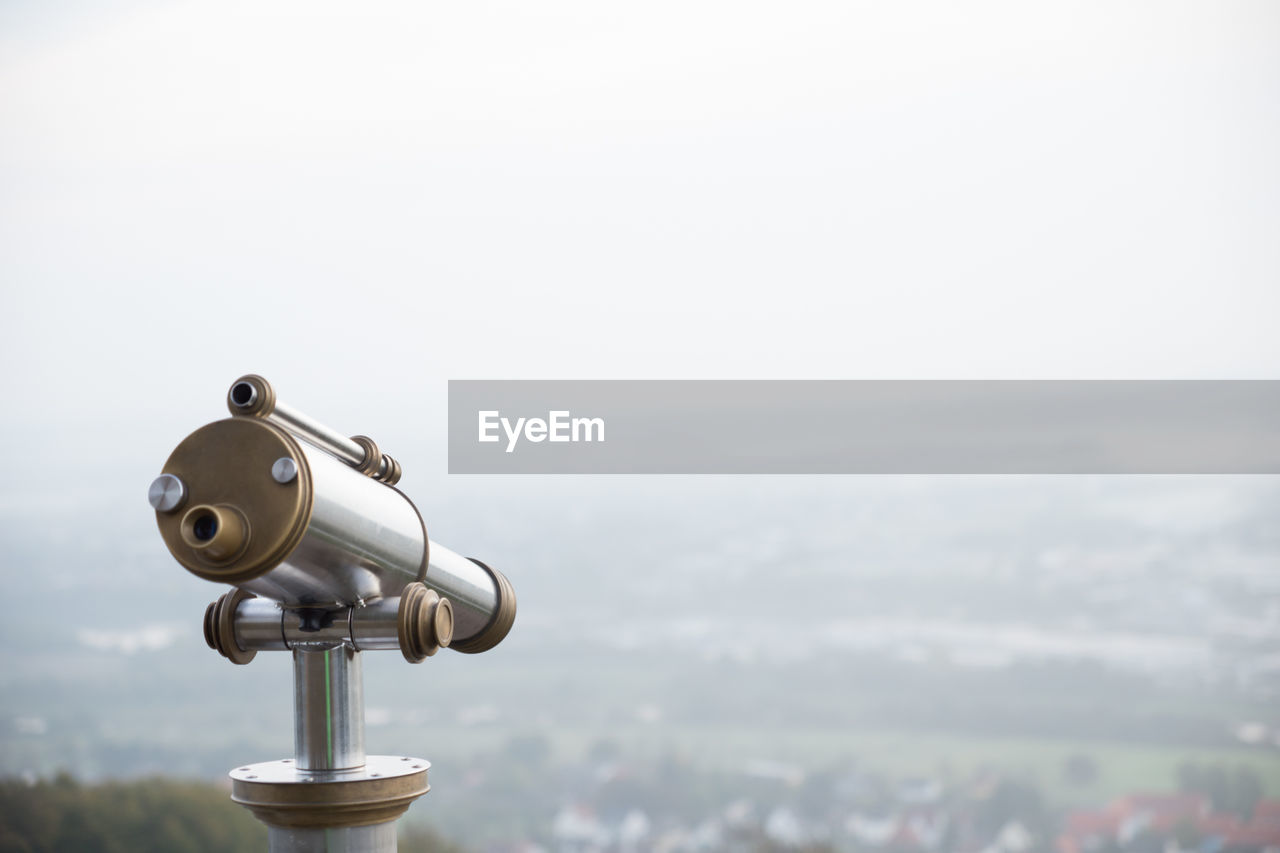 Close-up of hand-held telescope against cityscape during foggy weather