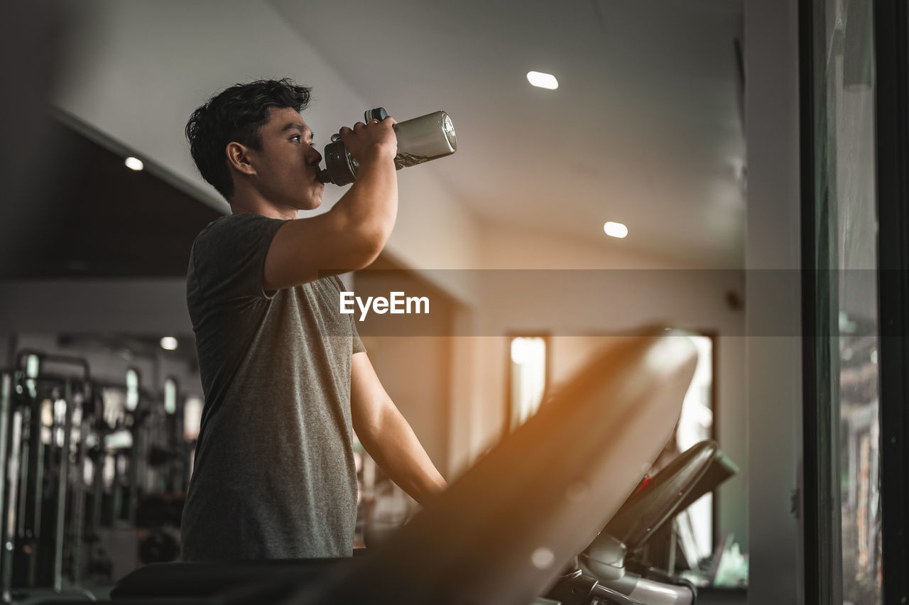 Young man drinking water while exercising in gym