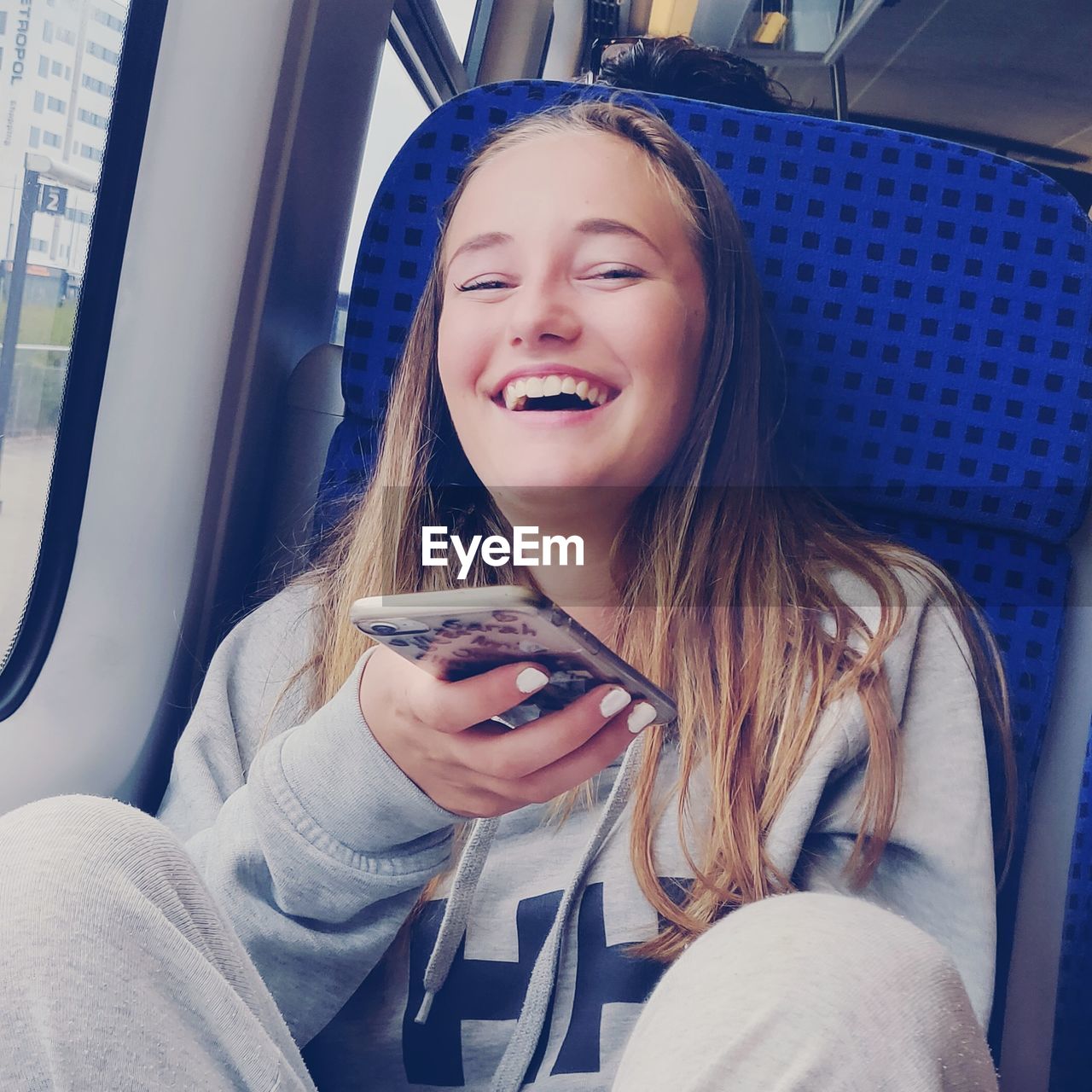 Cheerful teenage girl holding mobile phone while sitting in bus