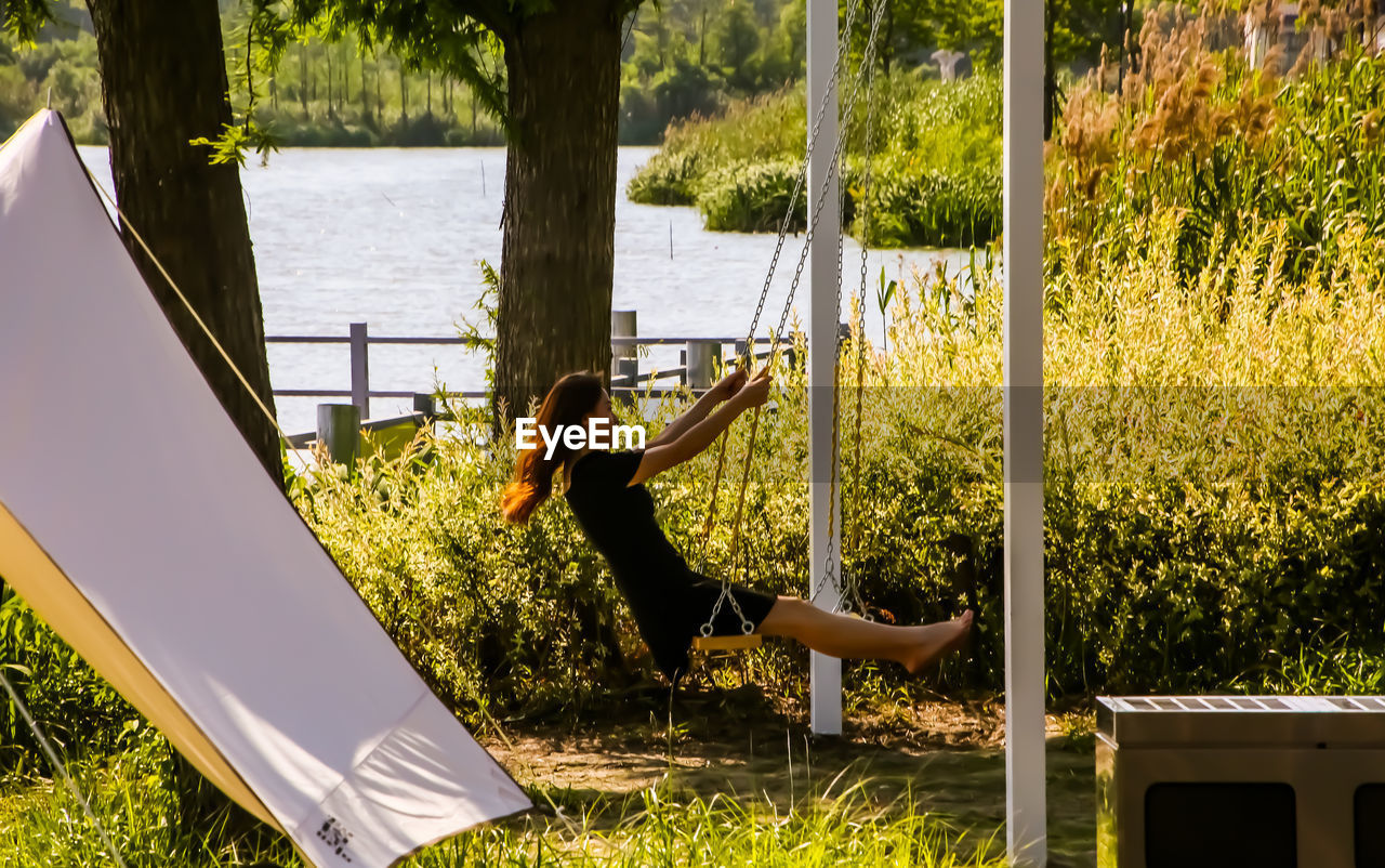 plant, one person, nature, full length, leisure activity, lifestyles, grass, sunlight, day, adult, tree, relaxation, yellow, outdoors, women, enjoyment, casual clothing, summer, water, young adult, men, backyard, playground, person, carefree, swing, fun, front or back yard