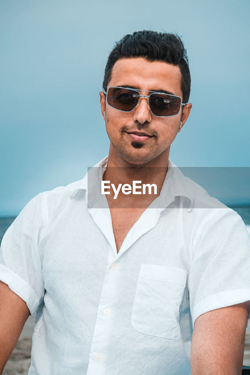 sunglasses, fashion, glasses, portrait, one person, adult, men, front view, waist up, blue, looking at camera, casual clothing, person, young adult, cool attitude, summer, clothing, eyewear, lifestyles, hairstyle, standing, photo shoot, day, sky, nature, relaxation, sea, button down shirt, leisure activity, water, outdoors, spring, emotion
