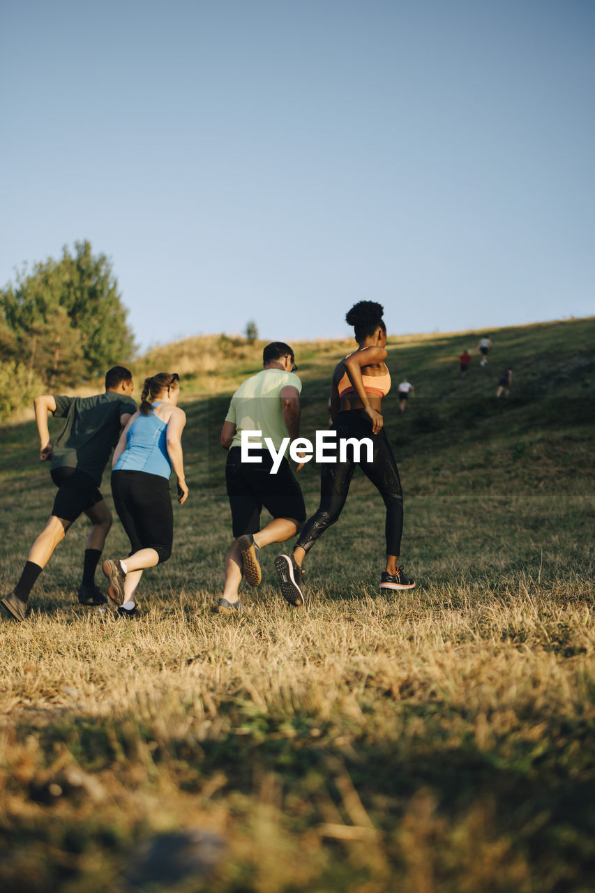 Rear view of male and female athletes running on grassy land