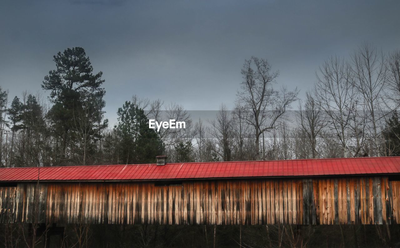 Covered bridge by trees against sky