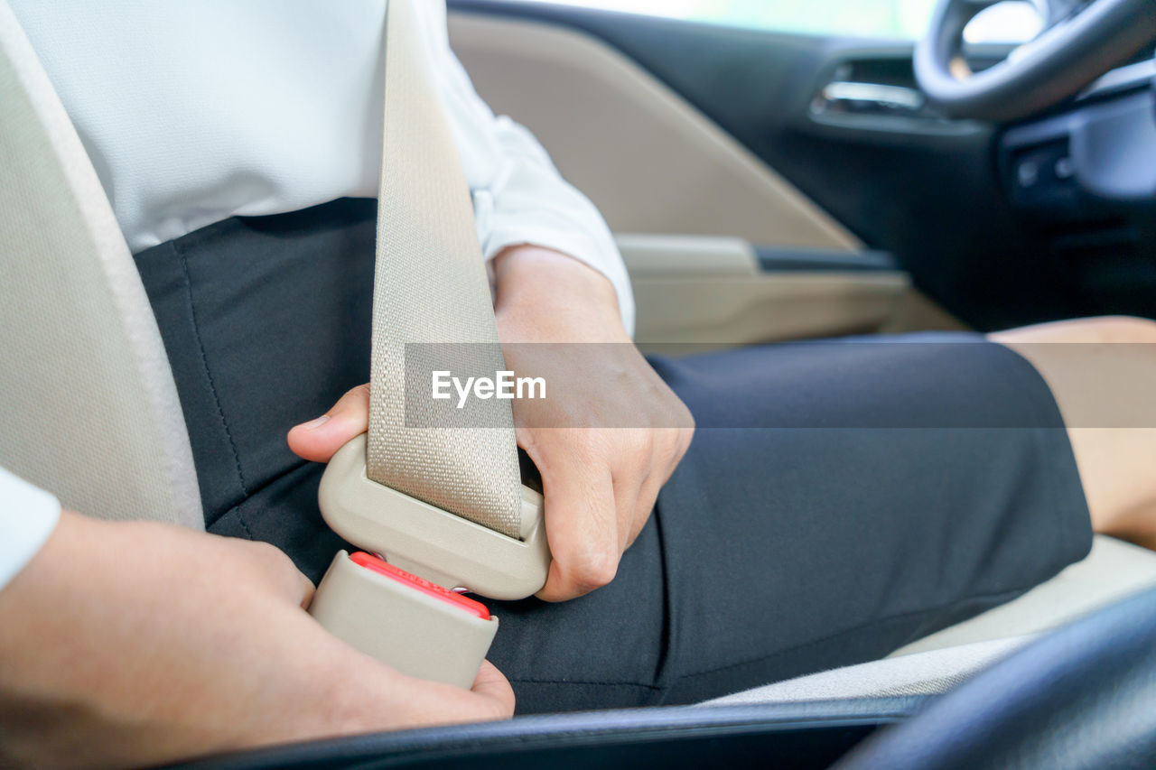 Midsection of businesswoman fastening seat belt while sitting in car