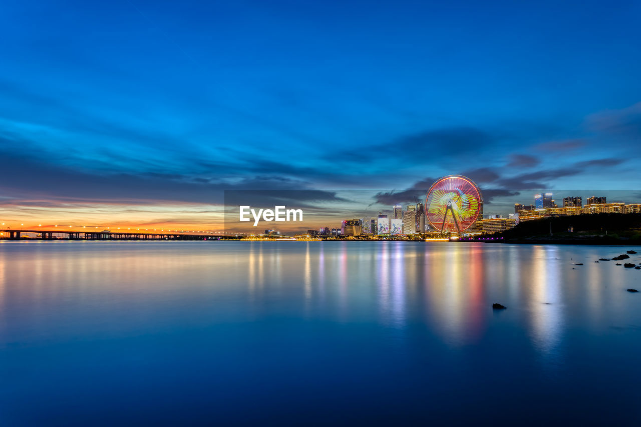 ILLUMINATED BRIDGE OVER SEA AGAINST BLUE SKY