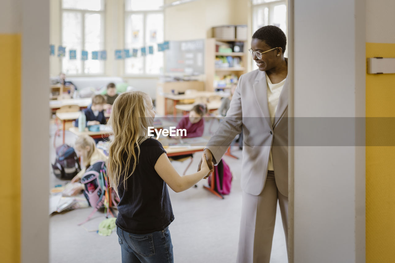 Smiling female teacher doing handshake with schoolgirl in classroom