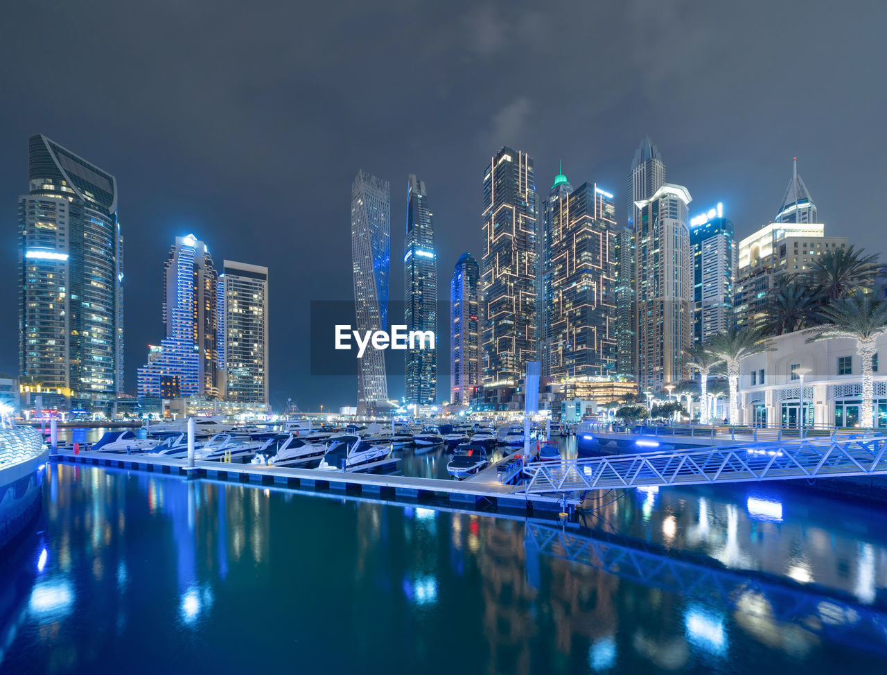 ILLUMINATED BUILDINGS BY SWIMMING POOL IN CITY AGAINST SKY