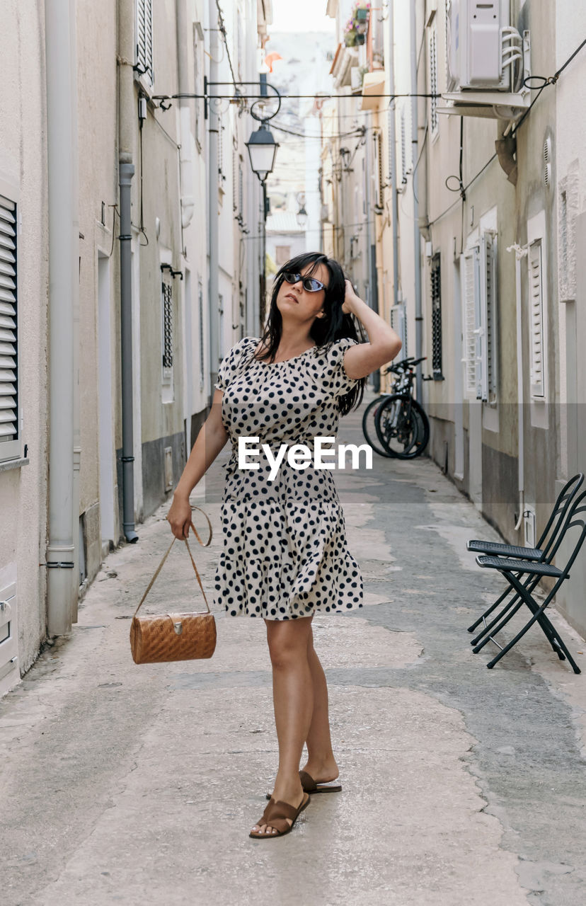 Portrait of attractive young woman standing in alley. summer dress, style, lifestyle.