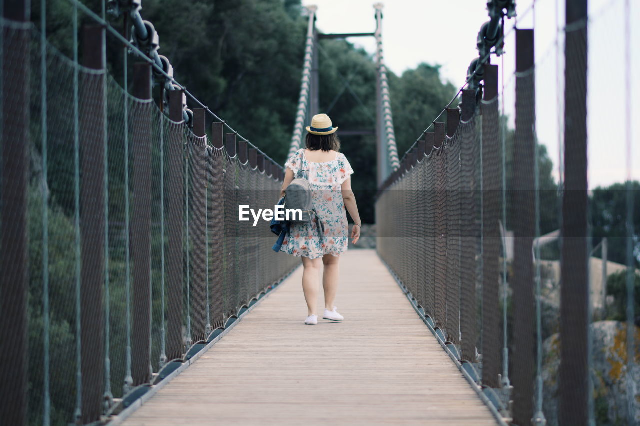 Rear view of woman walking on footbridge in forest