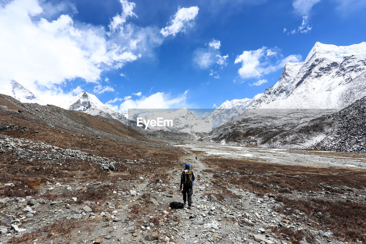 Rear view of person walking on landscape with snowcapped mountains in background