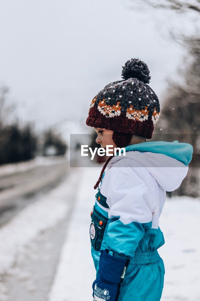 Side view of girl standing on snow covered field against sky