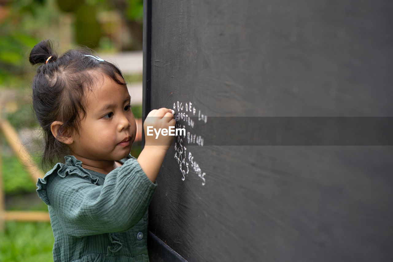 Portrait of cute girl writing alphabet on blackboard