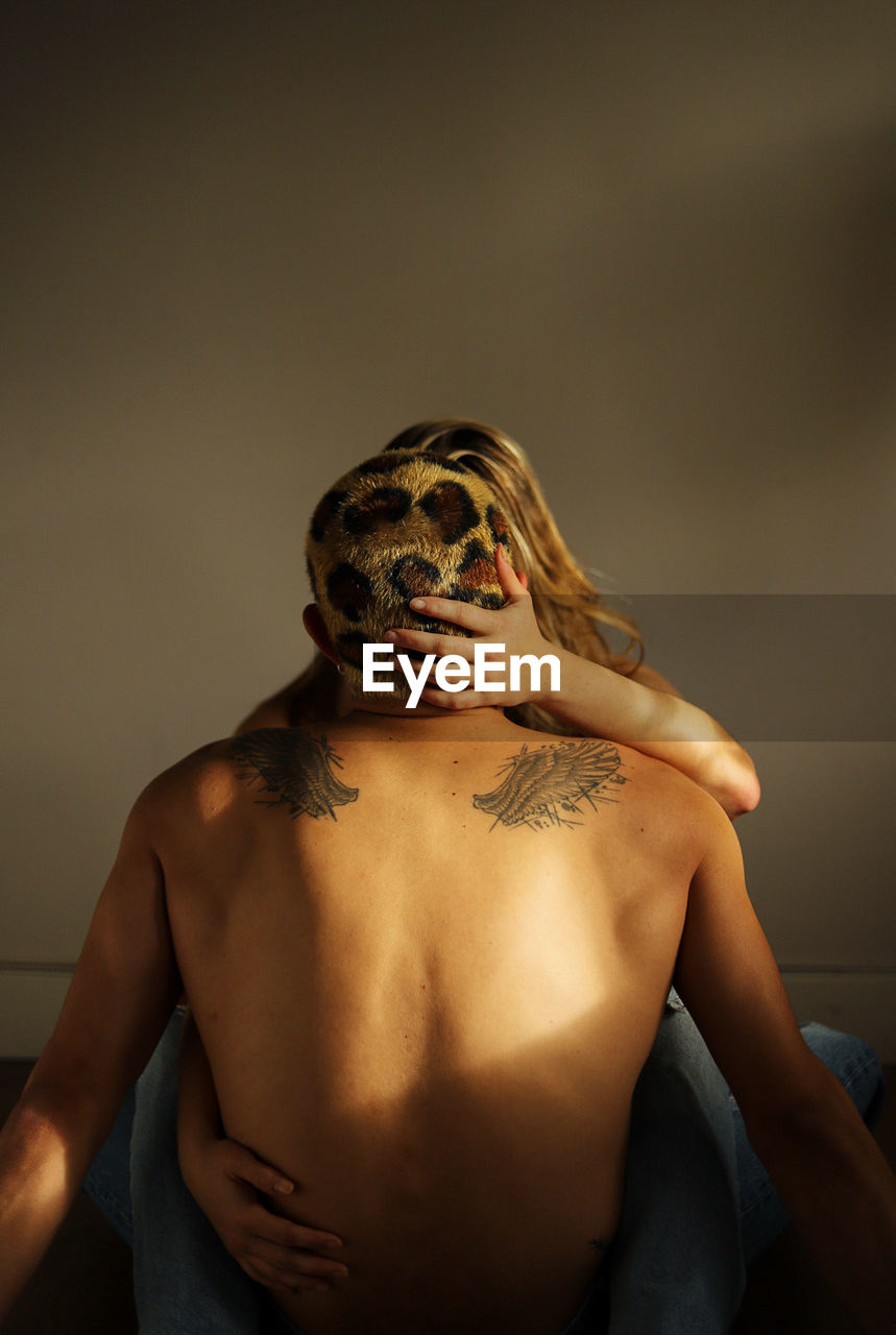 Young woman in casual clothes embracing shirtless boyfriend with dyed hair while sitting together in sunlit room at home