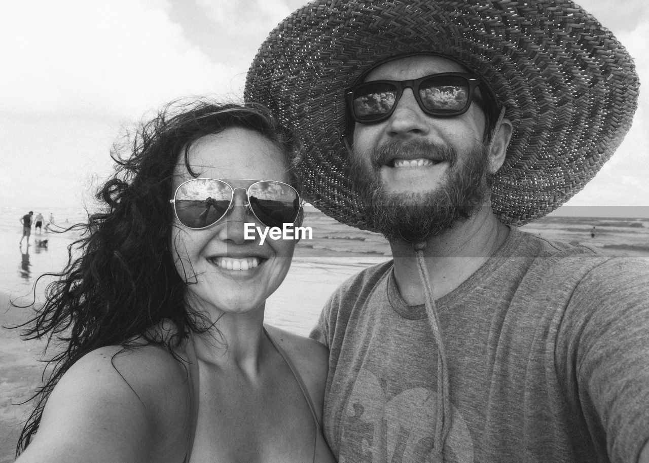 Portrait of smiling couple wearing sunglasses at beach