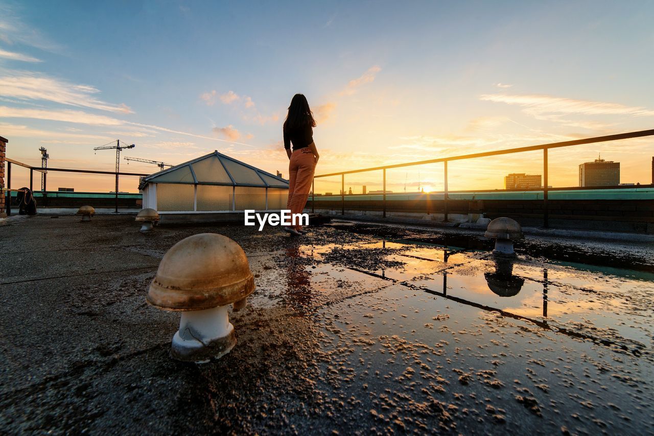 Rear view of woman looking at view from building terrace during sunset