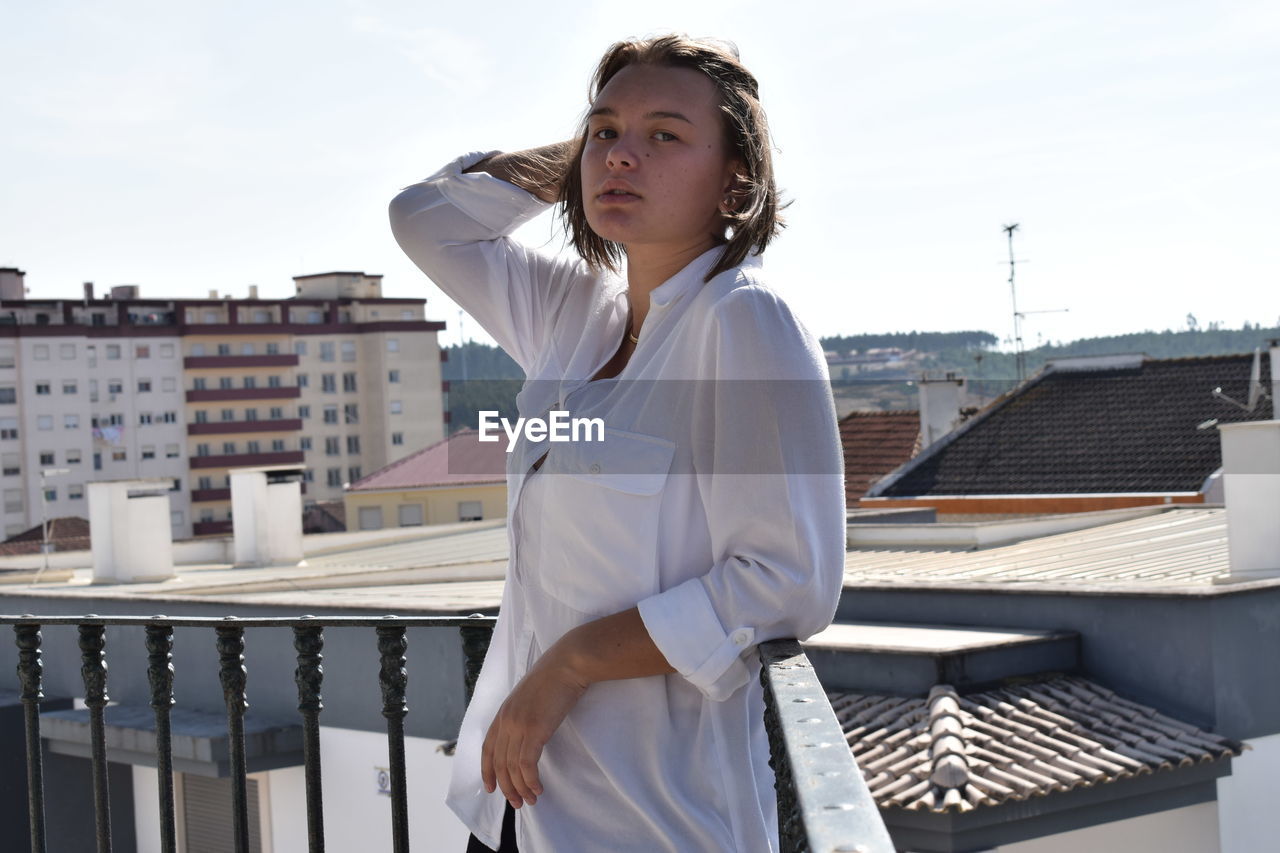 Portrait of young woman leaning on railing against buildings