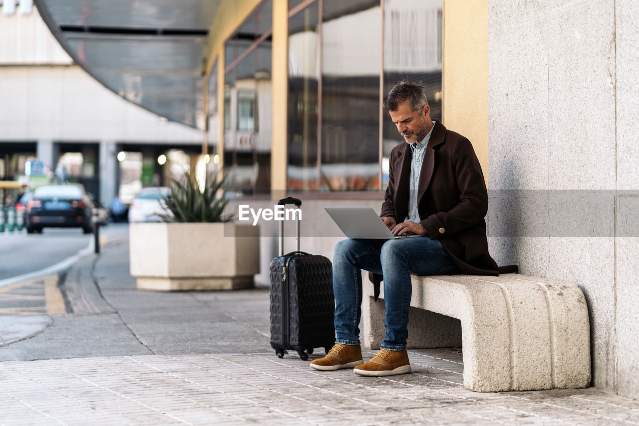 Full length of man using laptop while sitting on seat