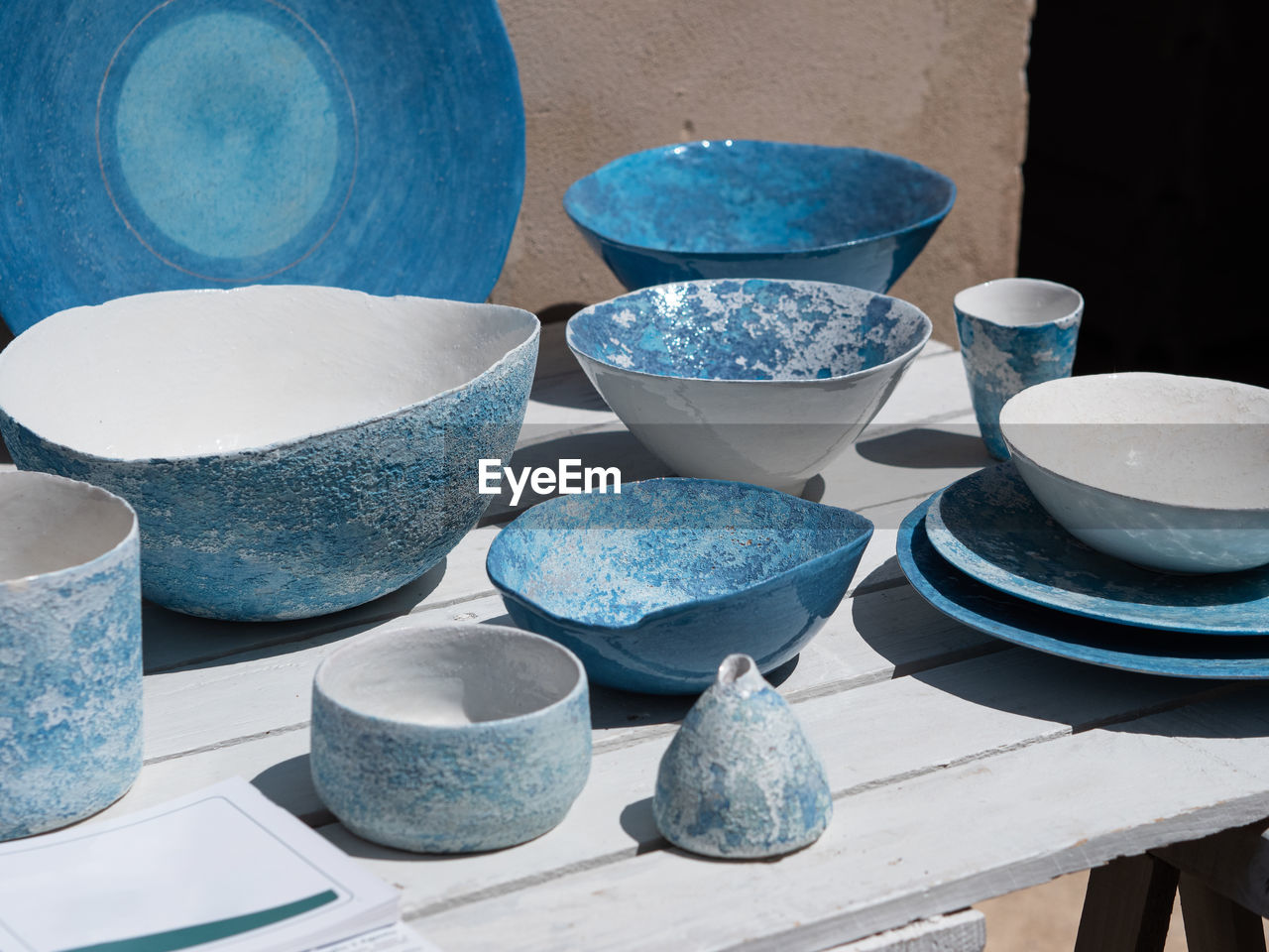 Blue and white ceramic plates, vases, and cups displayed on a wooden table outdoors.