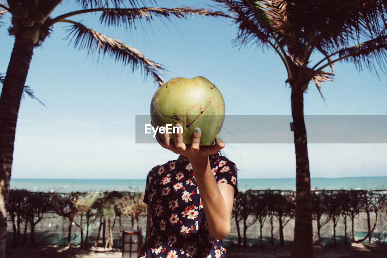Girl holding coconut in front of face at beach