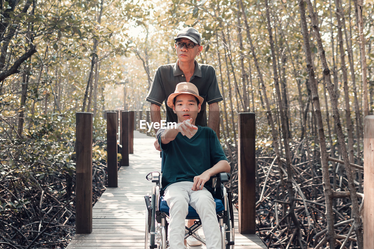 Father with disabled boy on wheelchair against trees