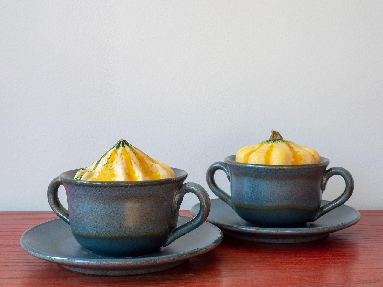 Close-up of small pumpkins placed in soup bowls on table against wall