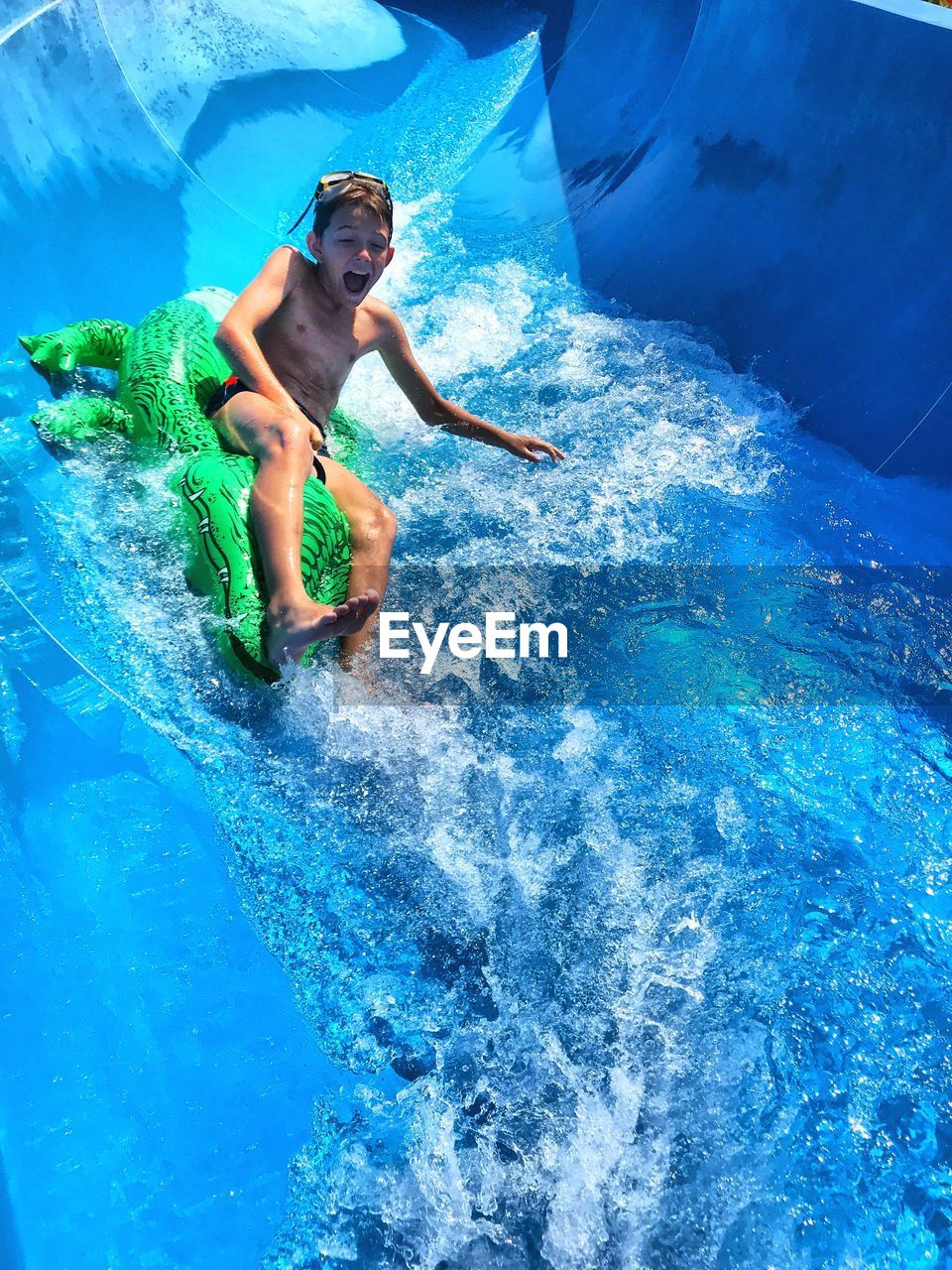 Playful boy sliding on water slide during sunny day