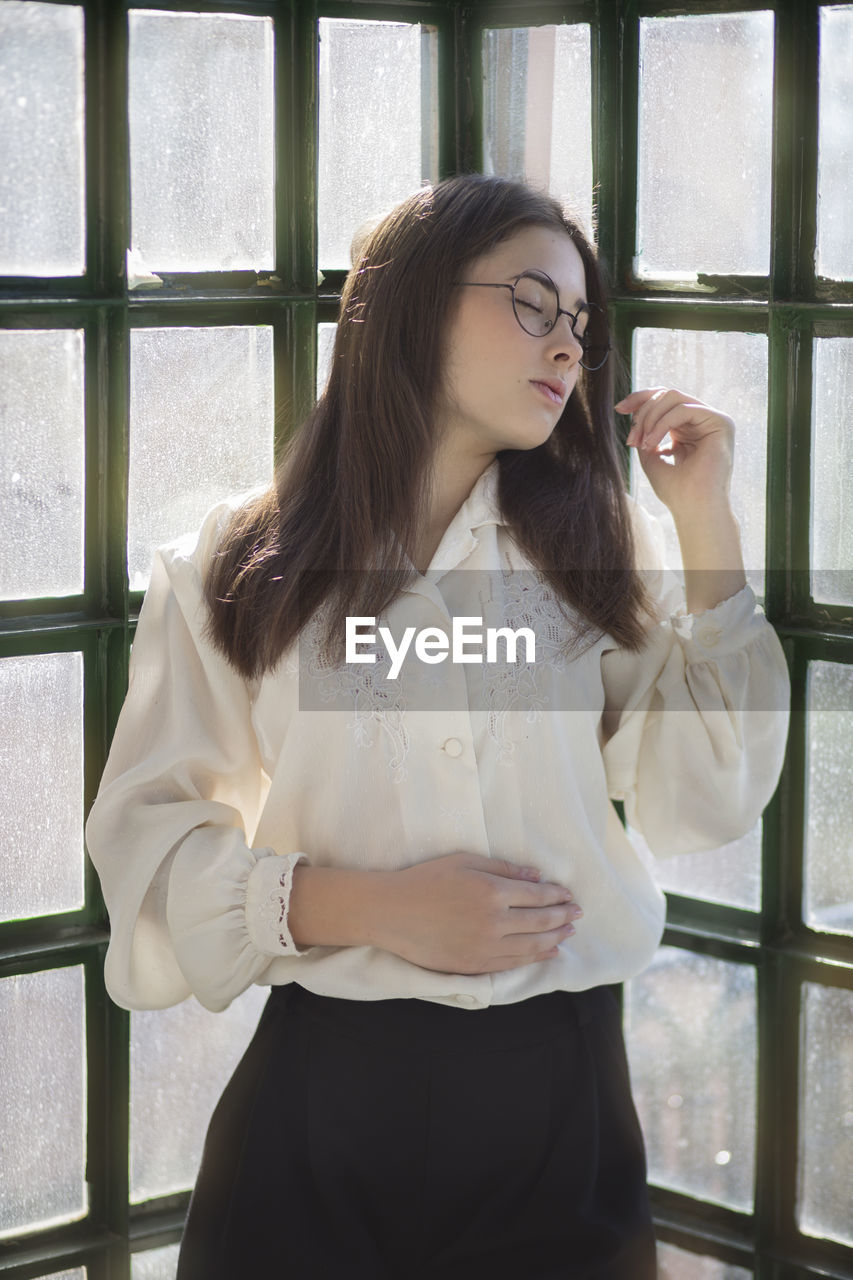 Portrait of romantic woman with vintage clothes and glasses leaning on a glass window