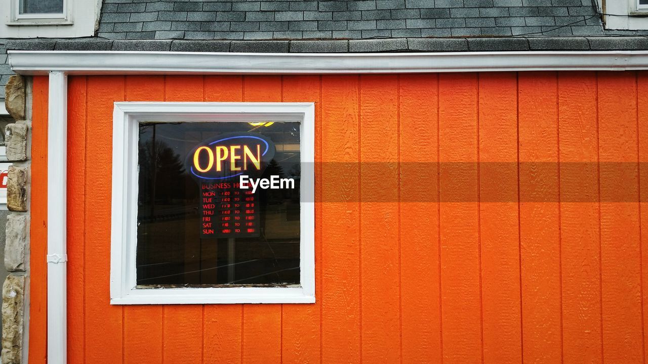Close-up of open sign on orange wall of shop