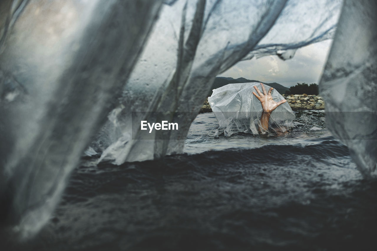 Cropped hand of person seen through plastic in lake