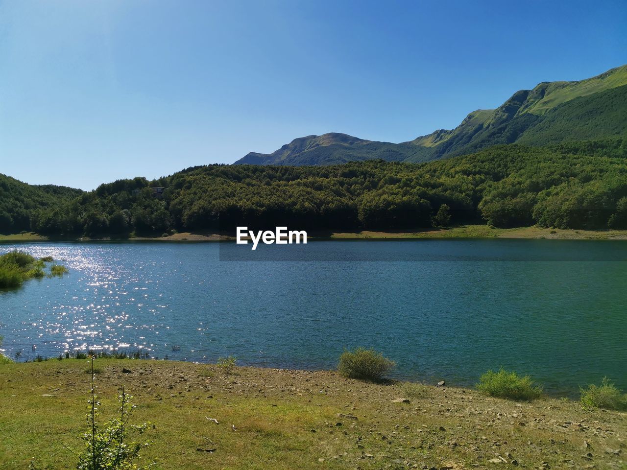 Scenic view of lake and mountains against clear blue sky