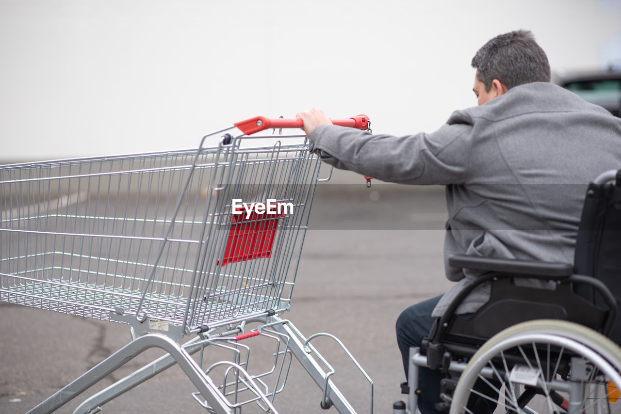 Physical disabled person in a wheelchair pushing shopping cart