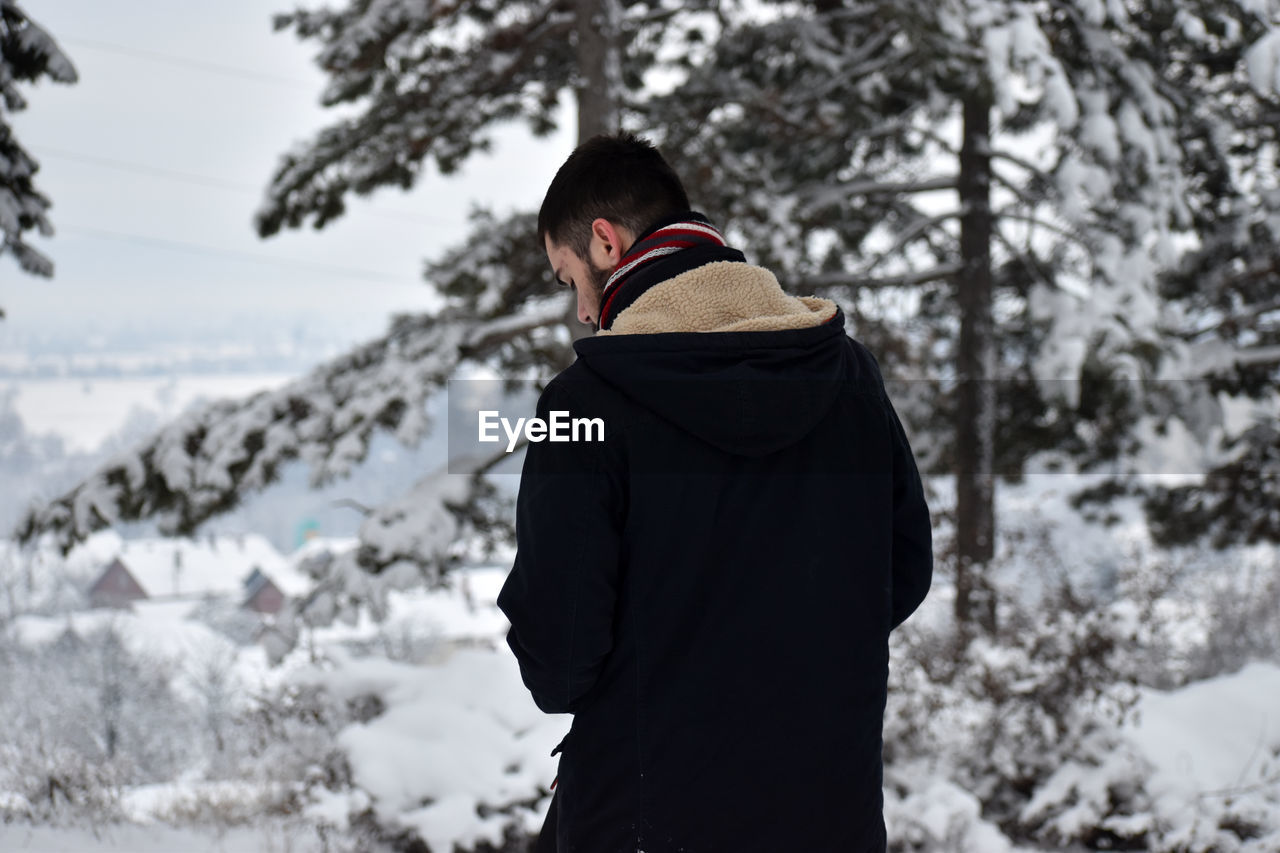 Rear view of man standing by tree during winter