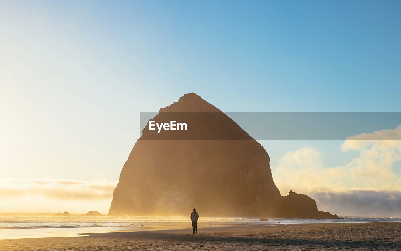 Man walking at beach against mountain and sky during sunrise