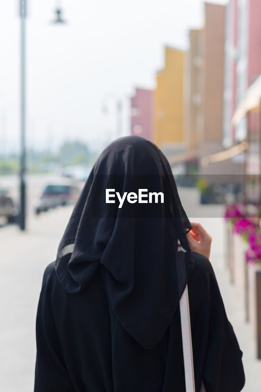Single muslim woman walks through empty big city, rear view.