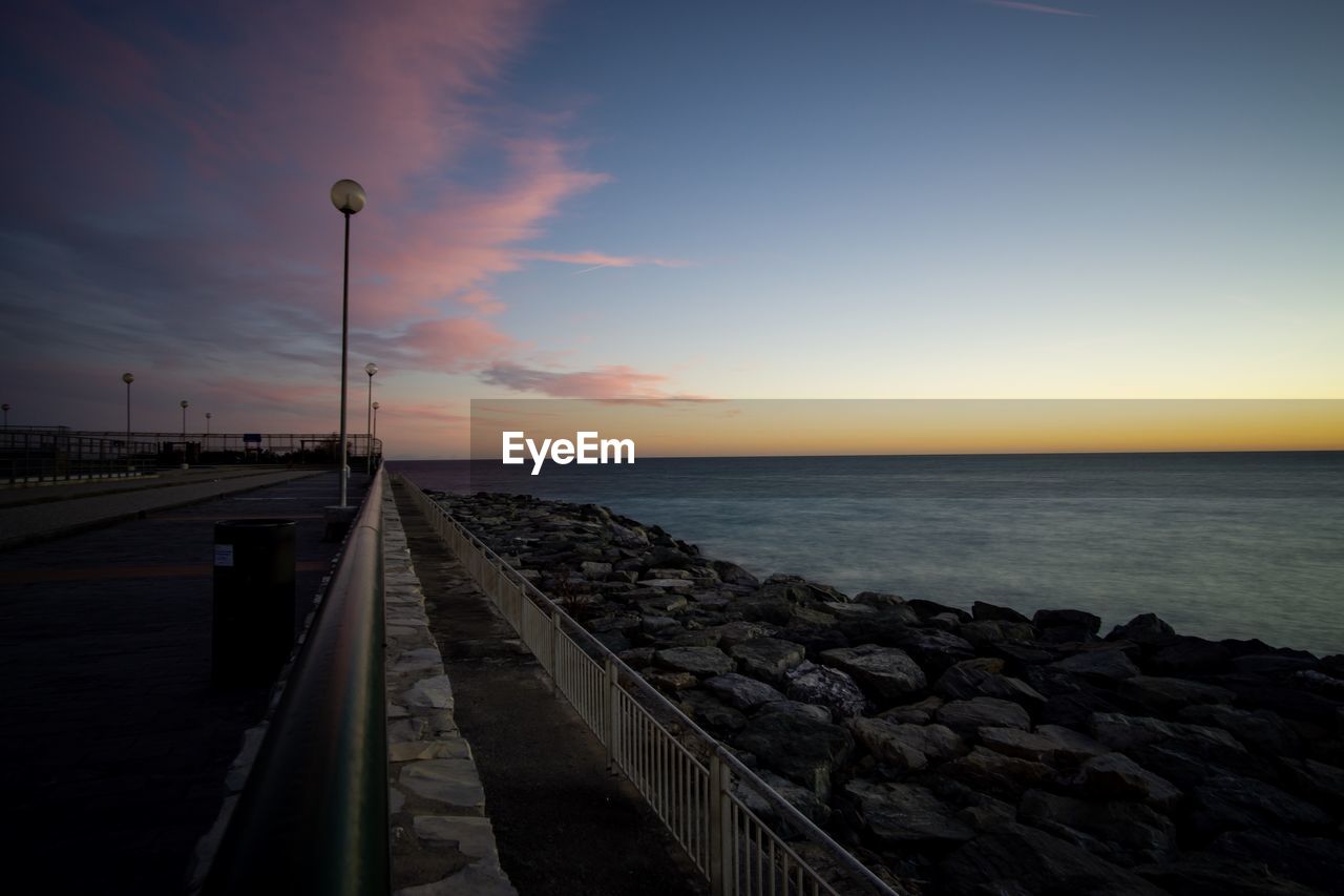 Street by sea against sky during sunset