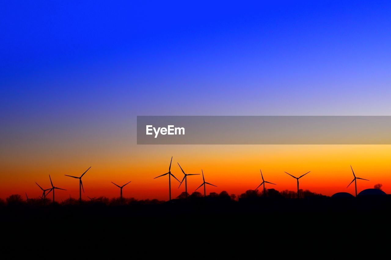 SILHOUETTE OF WIND TURBINES AGAINST ORANGE SKY