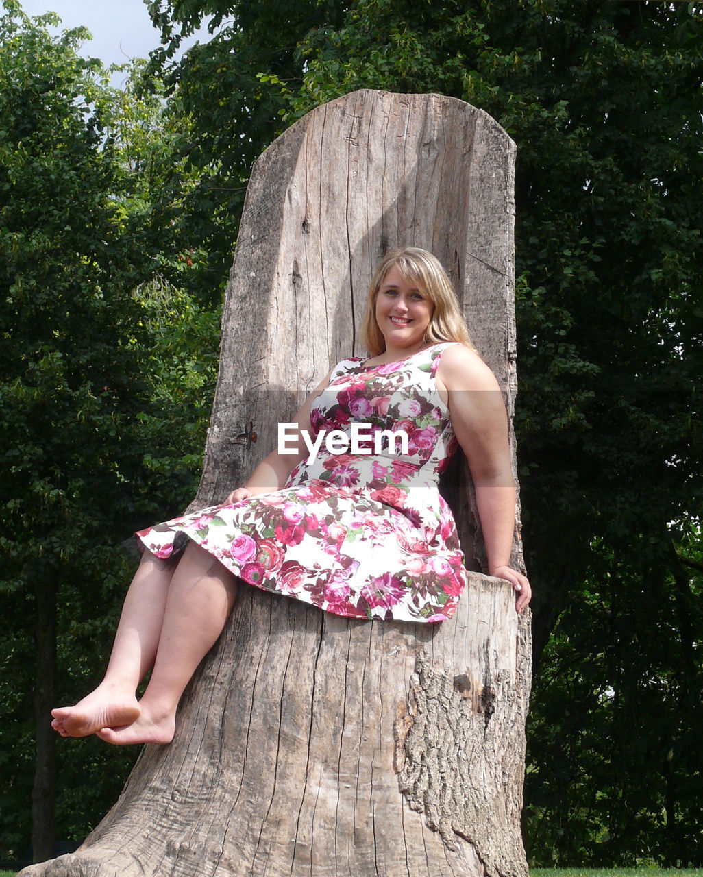 Portrait of woman sitting on tree stump in park