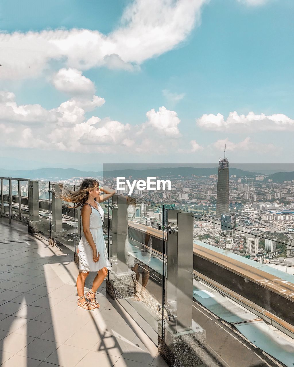 Side view of woman standing on balcony in city against sky